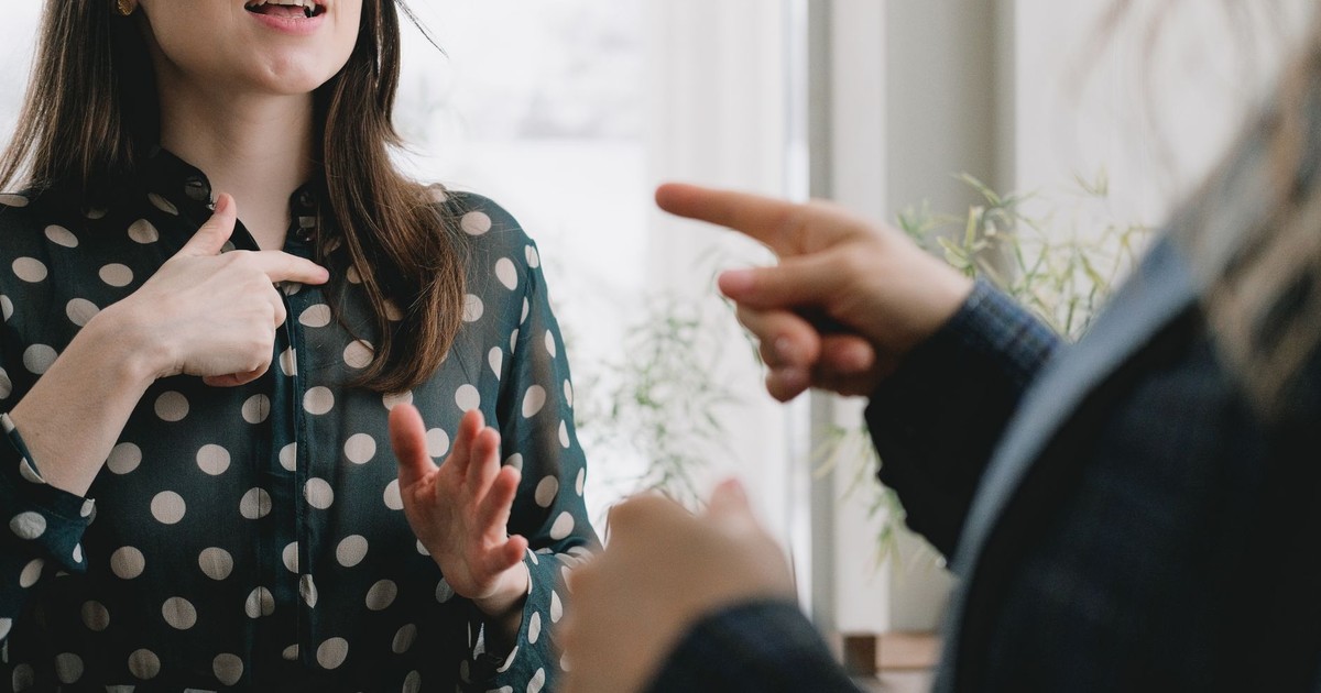 Crop unrecognizable woman in formal suit pointing at female colleague in elegant dress while standing together near window and discussing business plan in light office