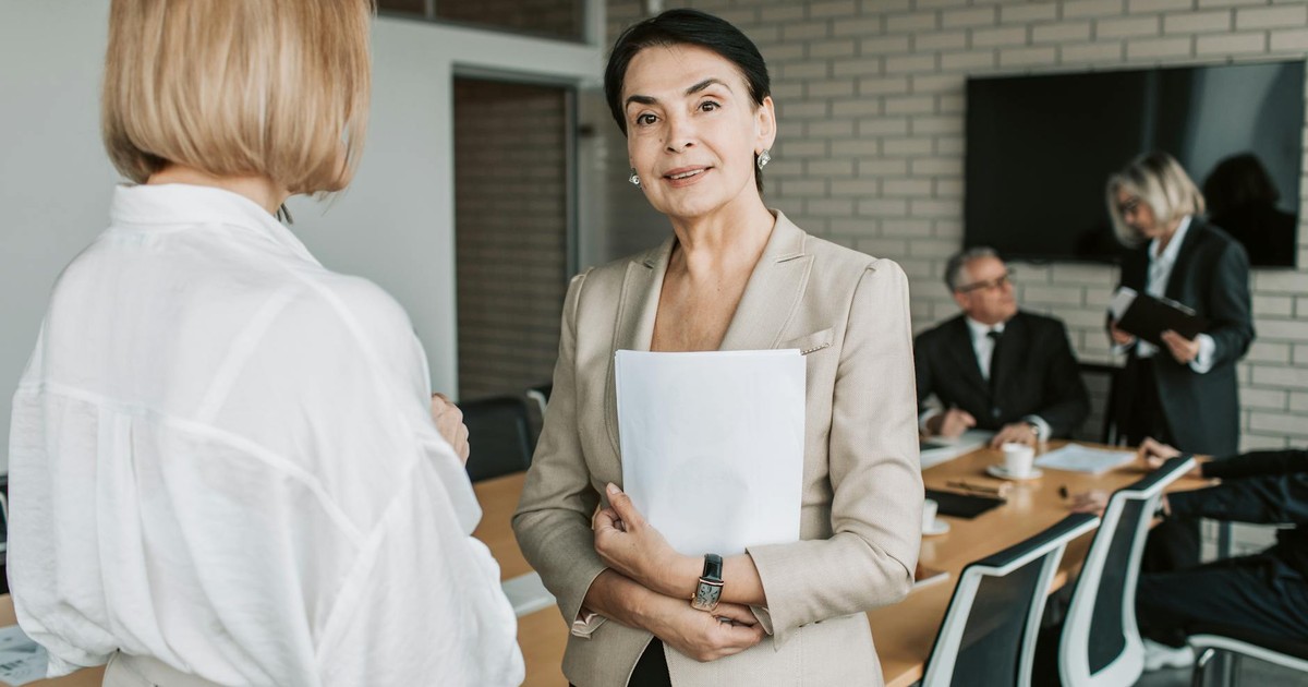 Senior businesswoman smiling and holding documents during a corporate meeting indoors.