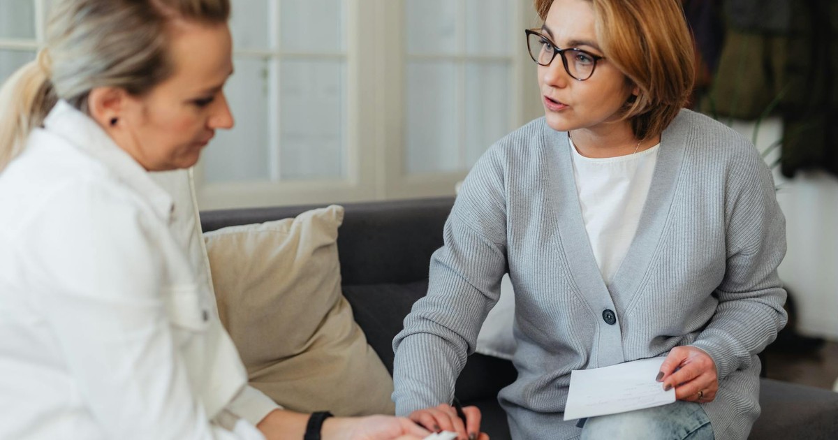 Two adult women sitting indoors having a thoughtful conversation on a couch.