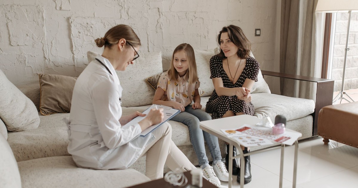 A doctor consults with a mother and daughter in a cozy indoor setting.