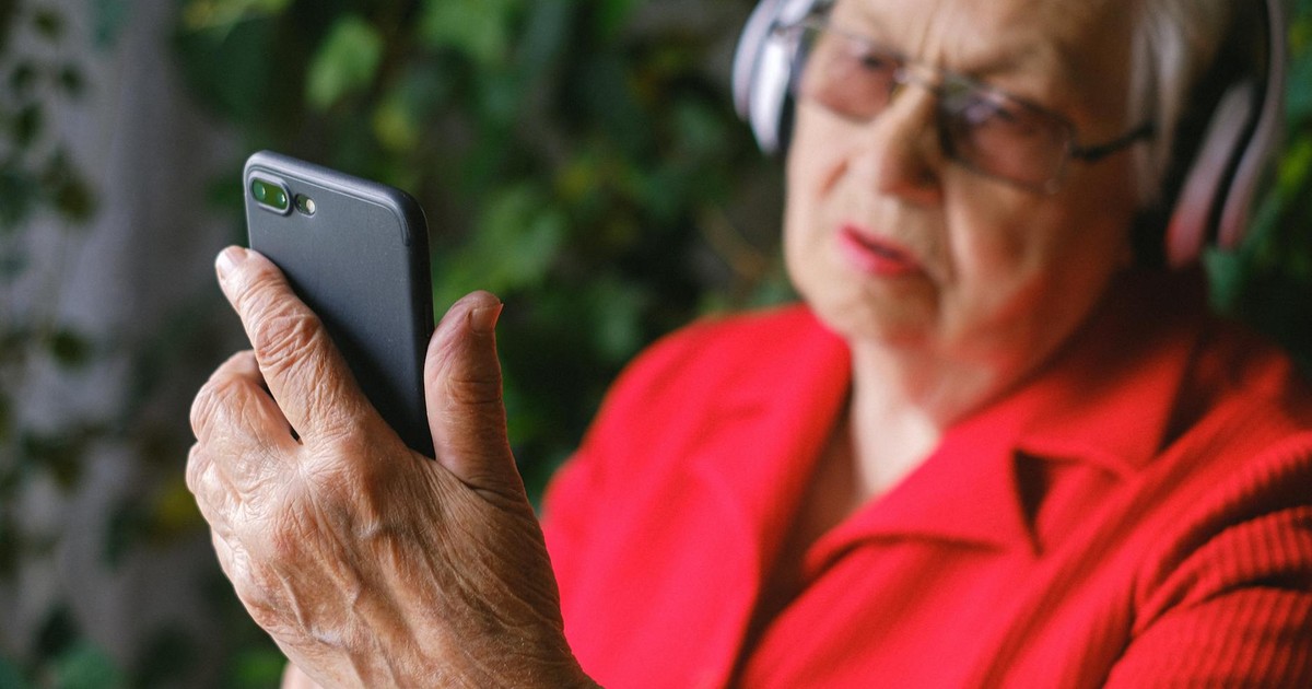 Senior woman in red using smartphone with headphones outdoors.