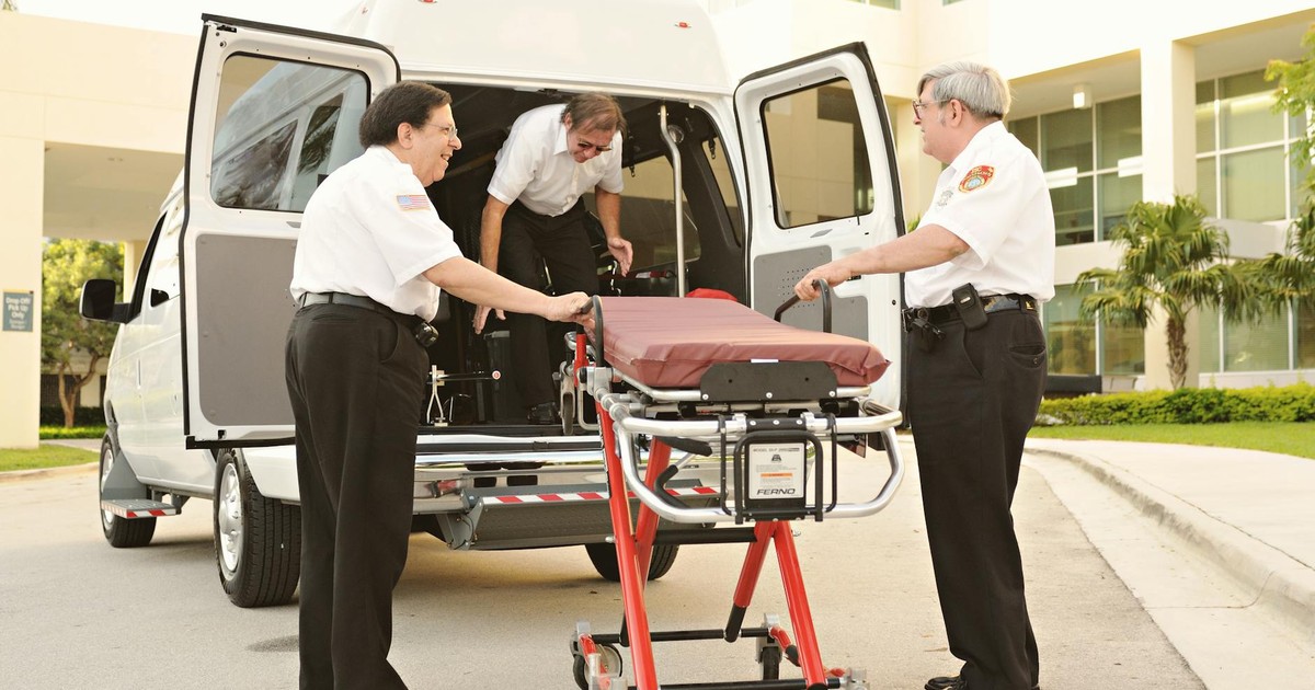Paramedics load a stretcher into an ambulance outside a medical facility.