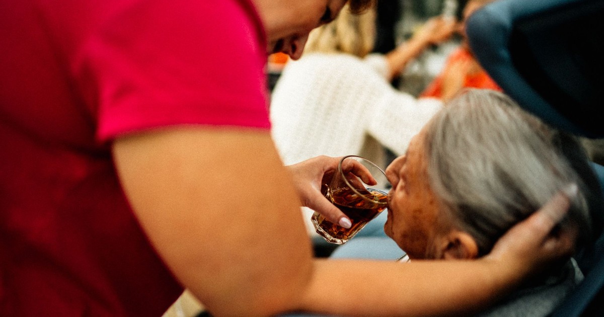 A caregiver helps an elderly woman drink tea, showcasing empathy and support.