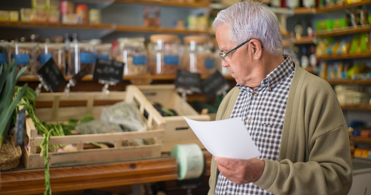 Senior man shopping in a Portuguese store, holding a shopping list.