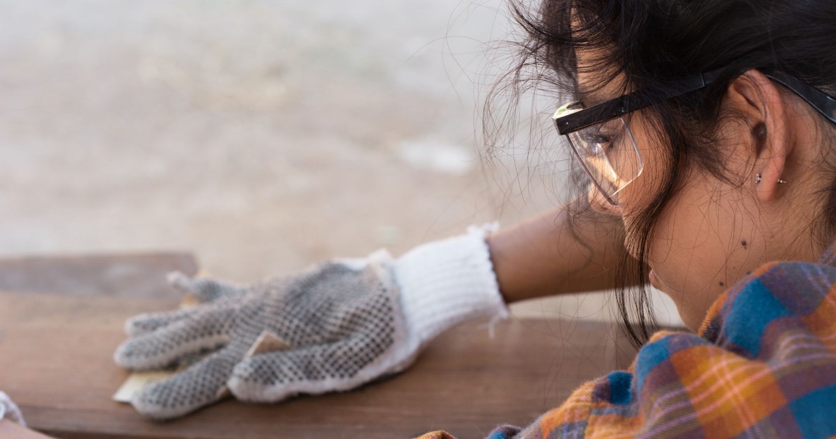 A woman in protective gear carefully sanding wood, focusing on detail and safety.