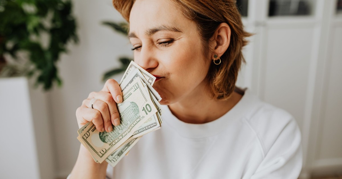 A woman joyfully smelling a handful of US dollar bills indoors.