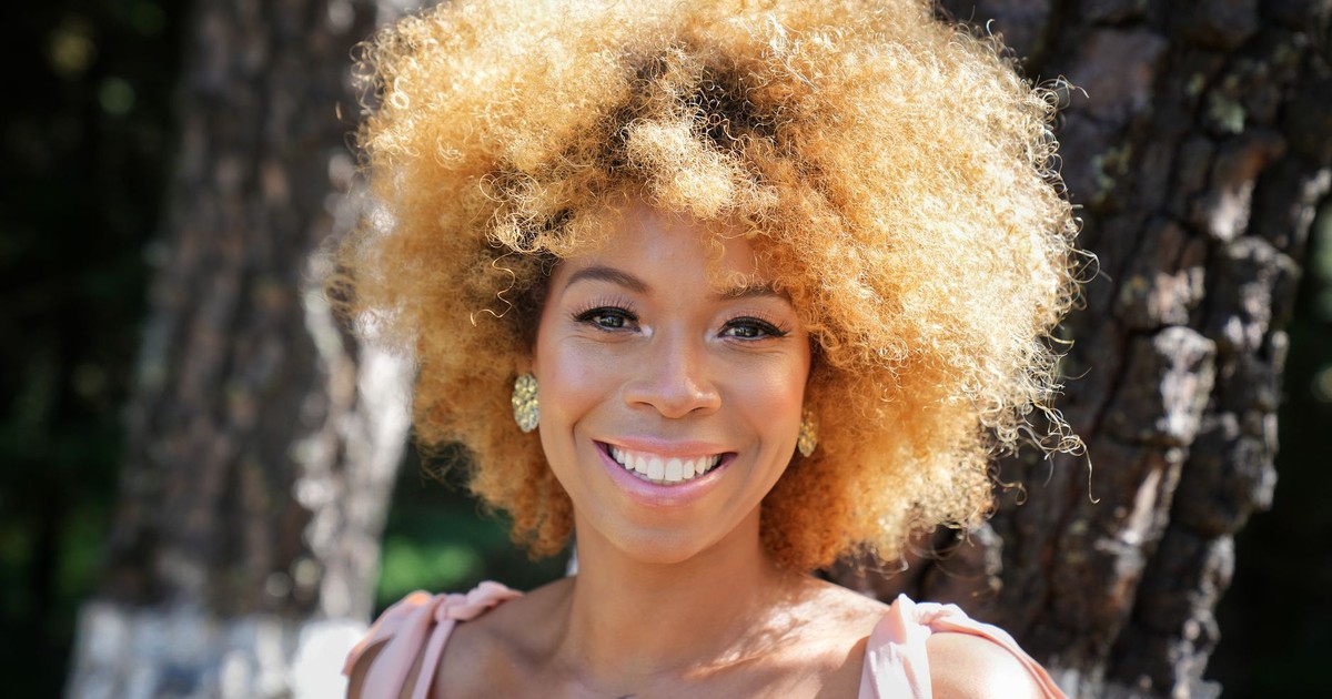 Portrait of a woman with curly hair smiling outdoors in a park setting.