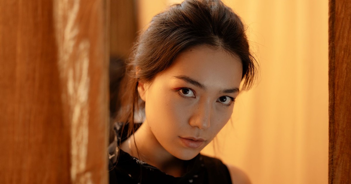 Close-up indoor portrait of a woman in warm lighting, gazing thoughtfully at the camera.