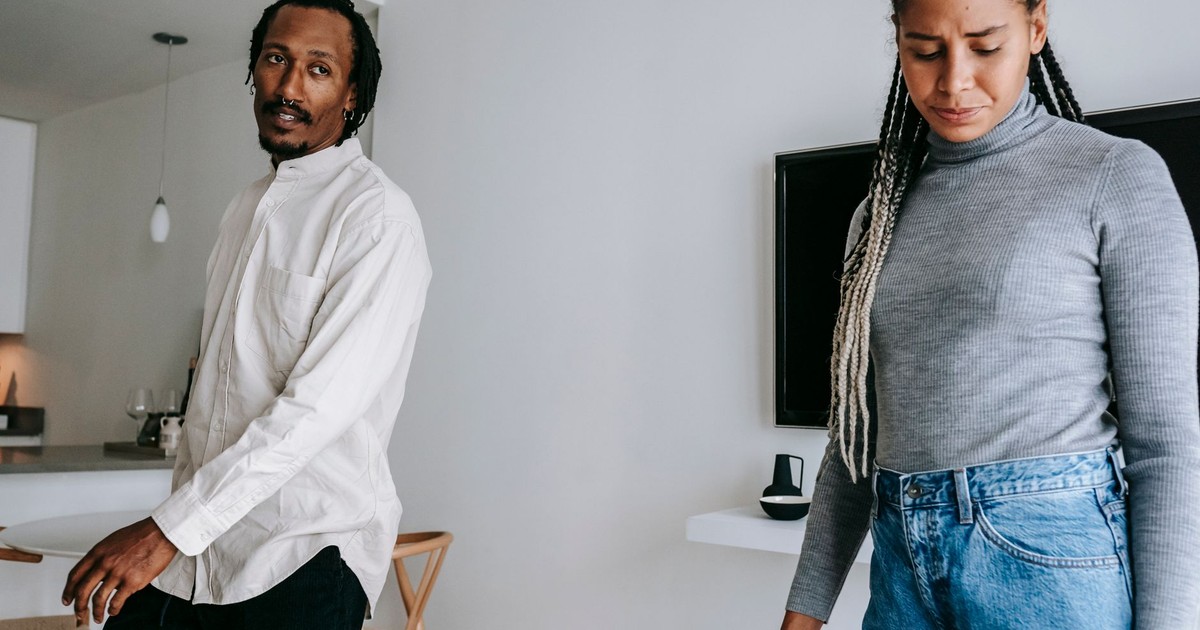 Concerned displeased African American couple in casual clothes having serious conversation in light living room