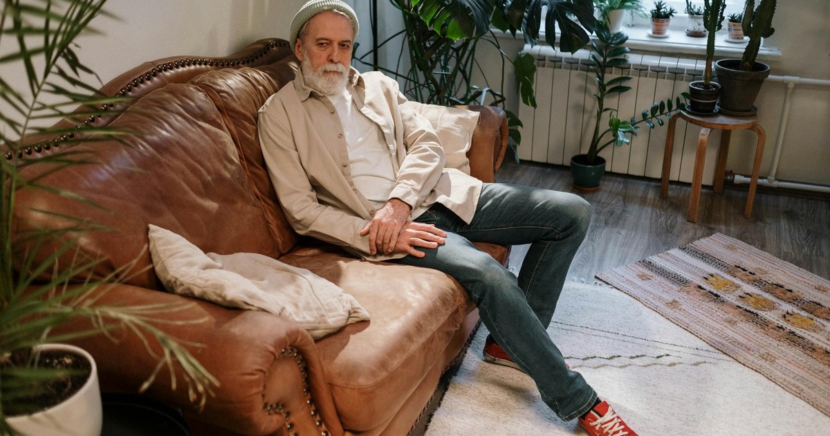 Elderly man relaxing on a leather sofa in a cozy indoor setting with plants.