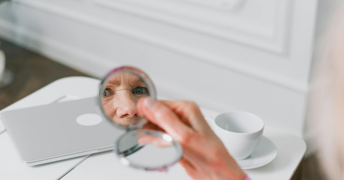 Close-up of a senior woman holding a pocket mirror, reflecting her face indoors.