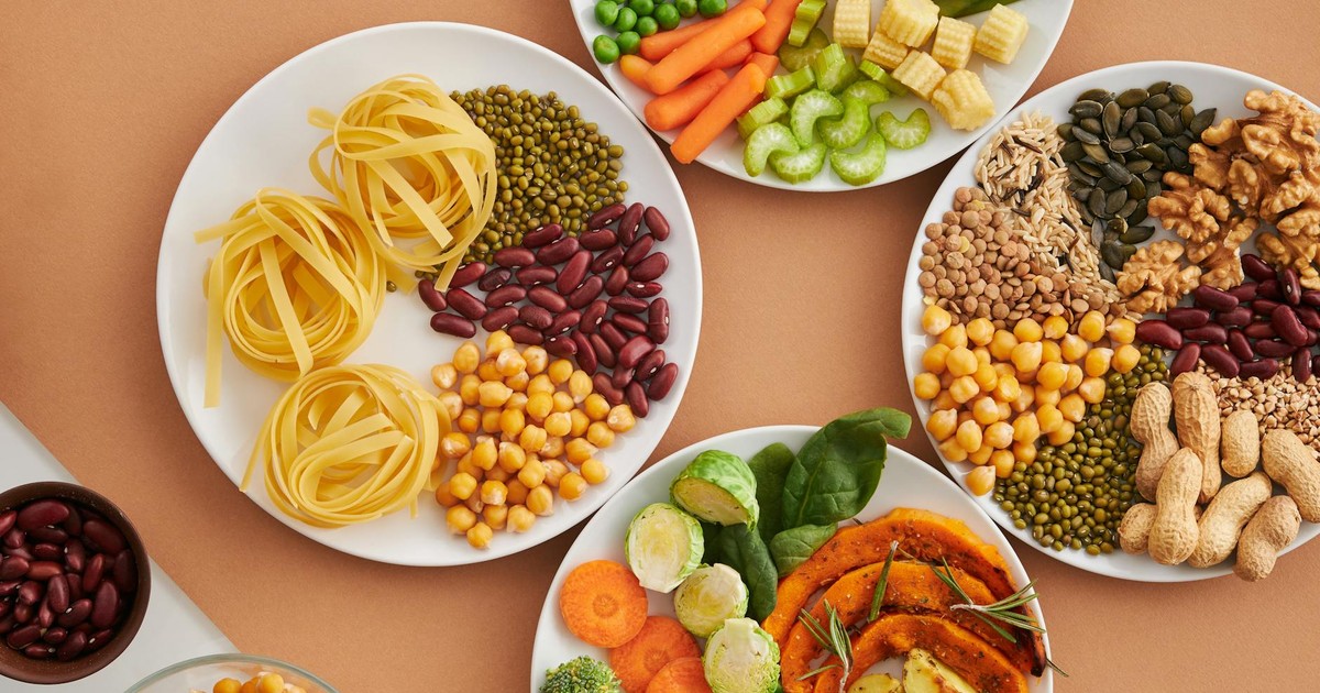 A vibrant mix of legumes, vegetables, nuts, and pasta arranged on white plates showcasing a balanced, healthy diet.