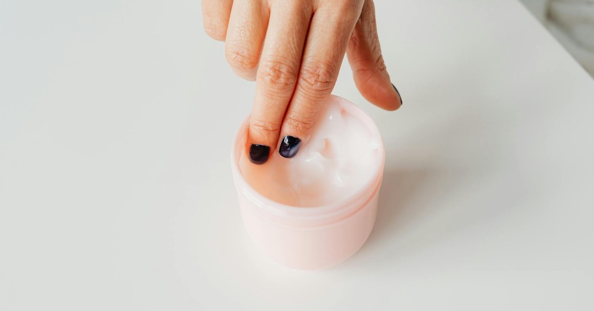 Close-up of a hand with painted nails dipping into a jar of face cream, representing self-care.
