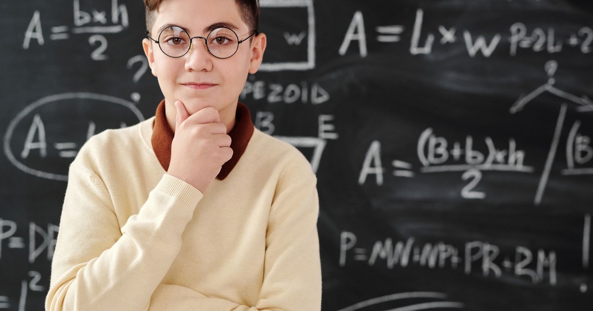 Smart student in glasses posing confidently in front of a blackboard full of mathematical equations.