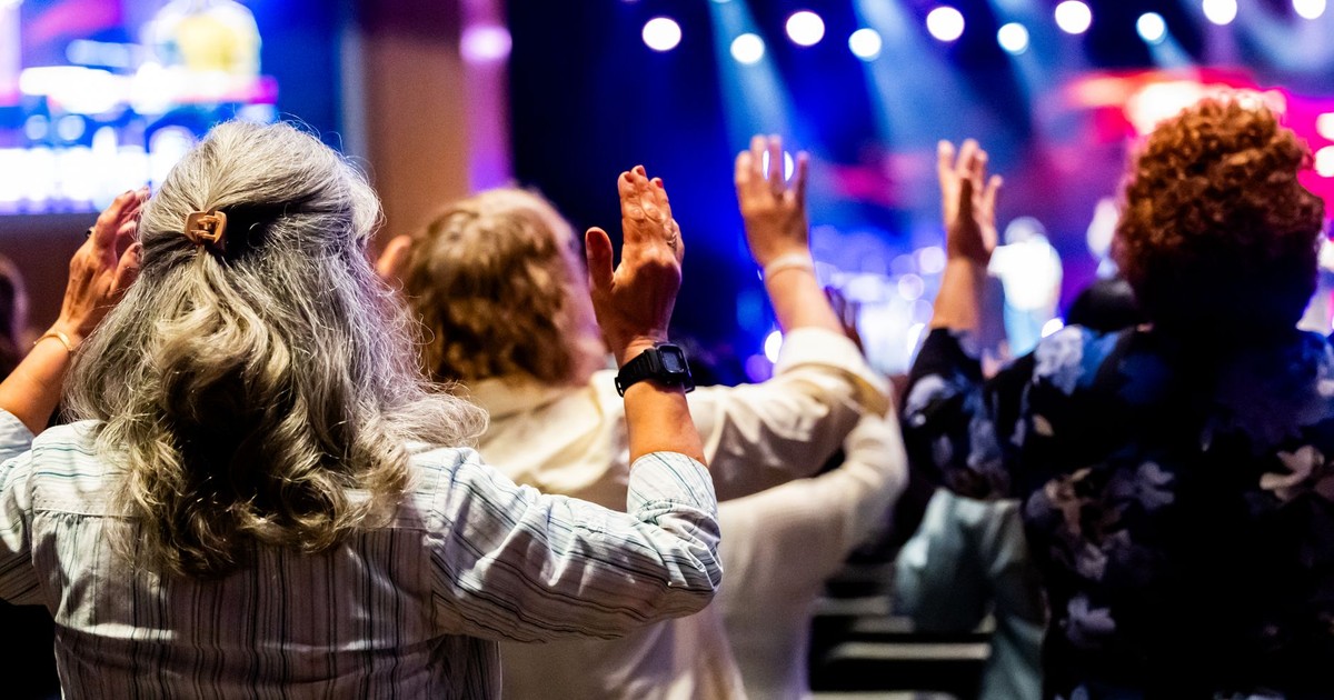 A group of people with raised hands attending a lively worship service inside a church.