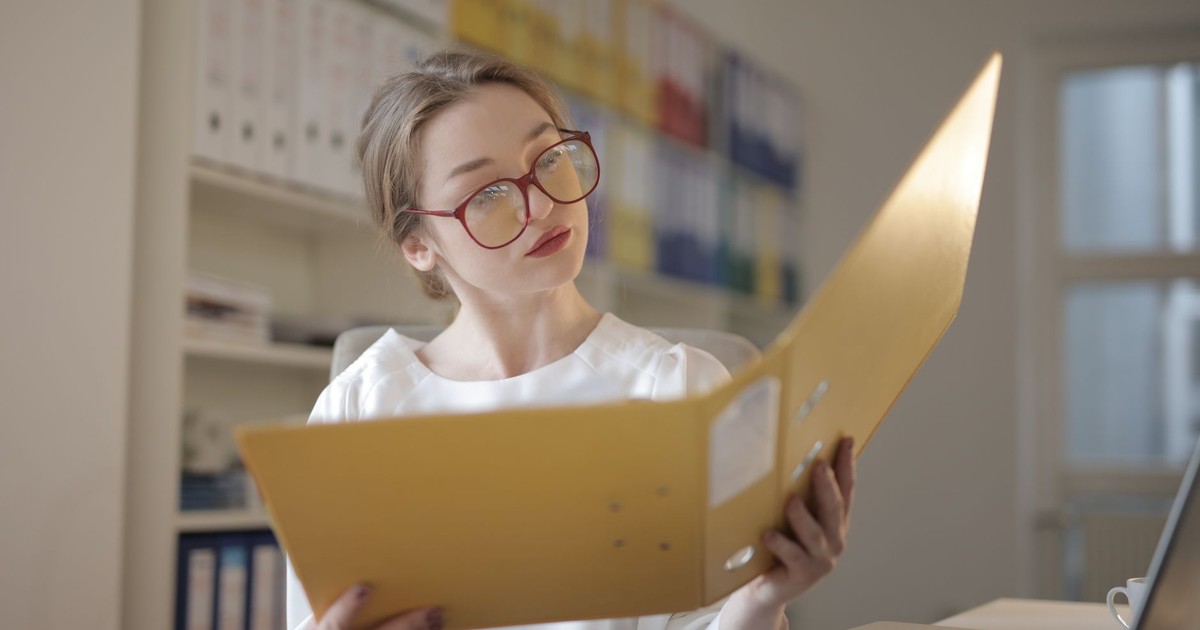 Caucasian woman intensely reading documents in an office setting.