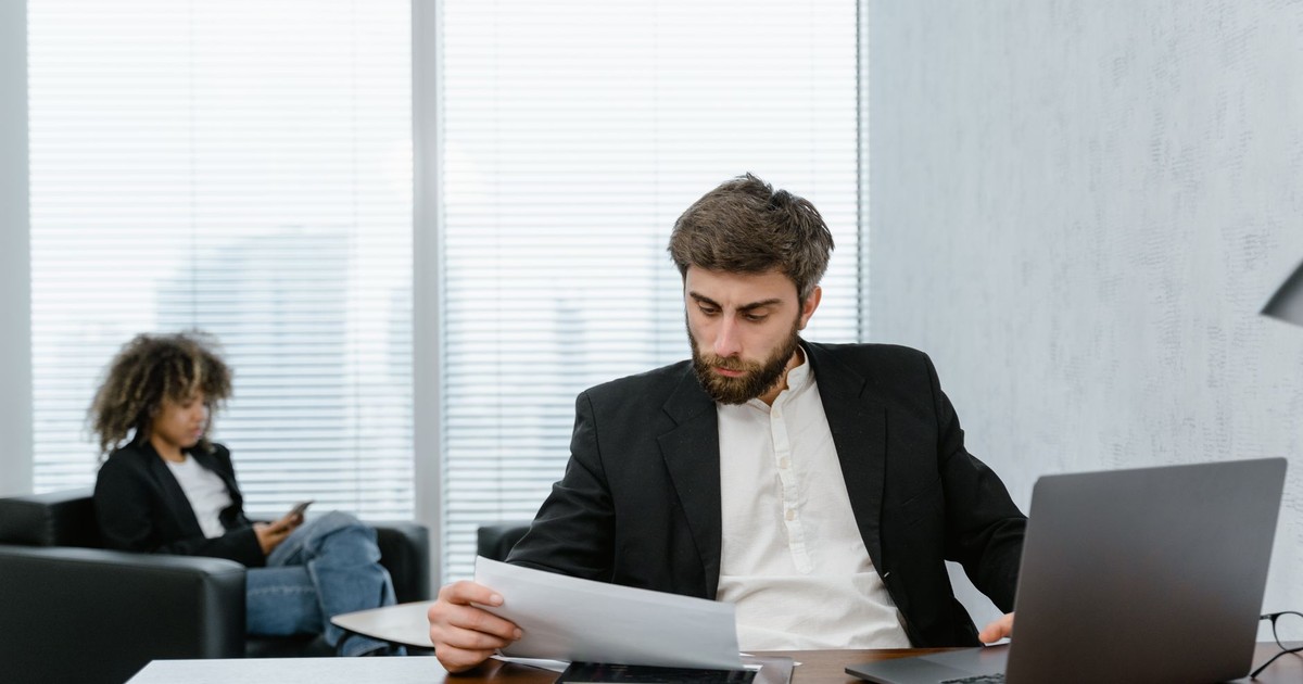 Focused businessman reviews financial reports at office desk with laptop.