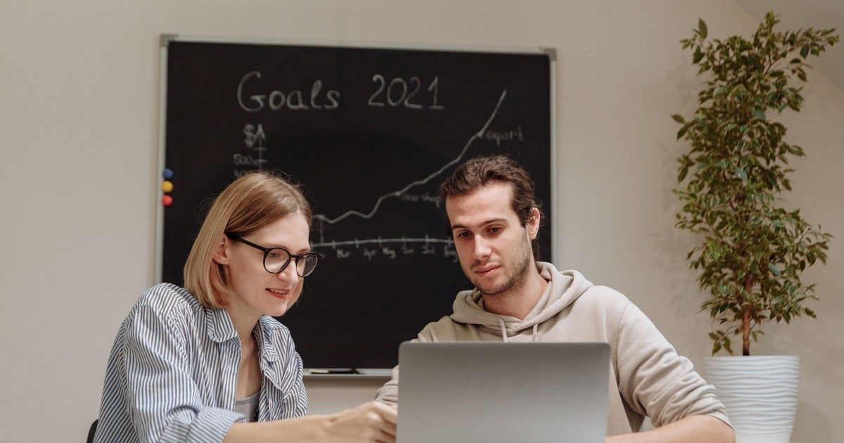 Two coworkers collaborating on 2021 goals in a modern office setting with a laptop.