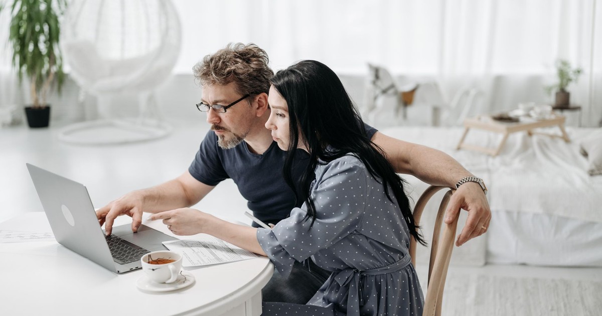 A man and woman sitting indoors, collaborating on a laptop at a table with coffee.
