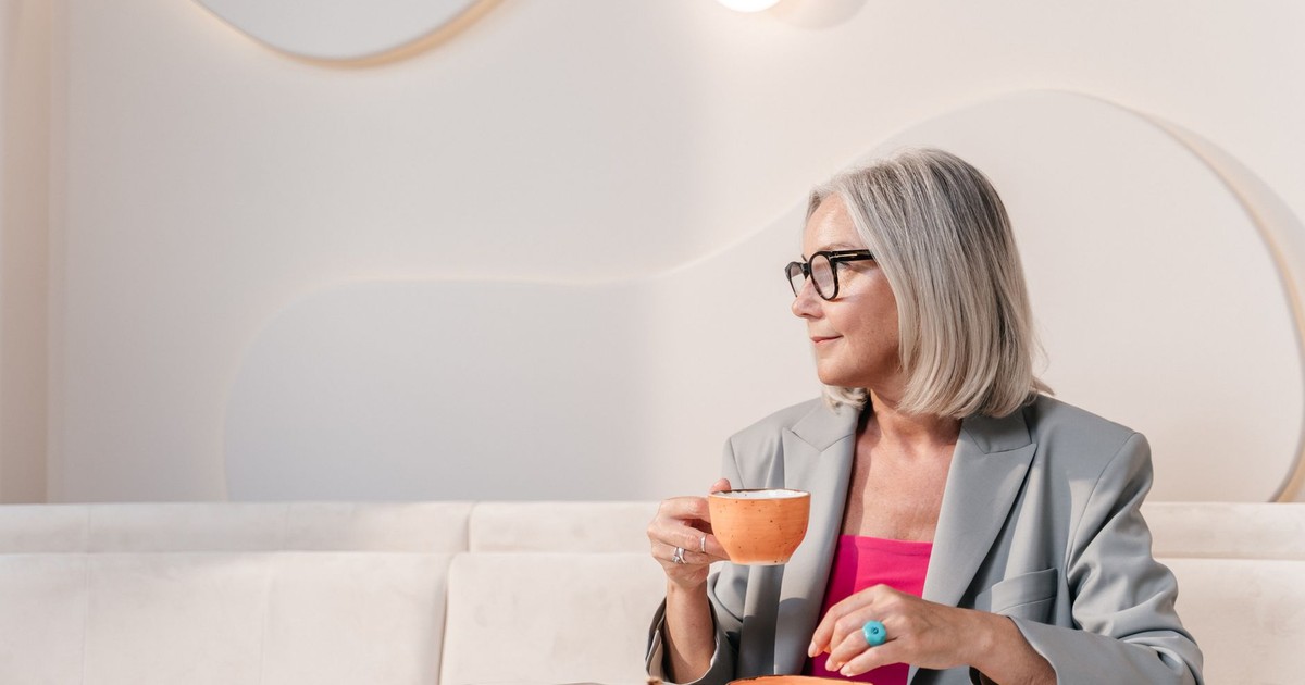 Sophisticated woman in blazer savoring coffee in a chic minimalist cafe setting.
