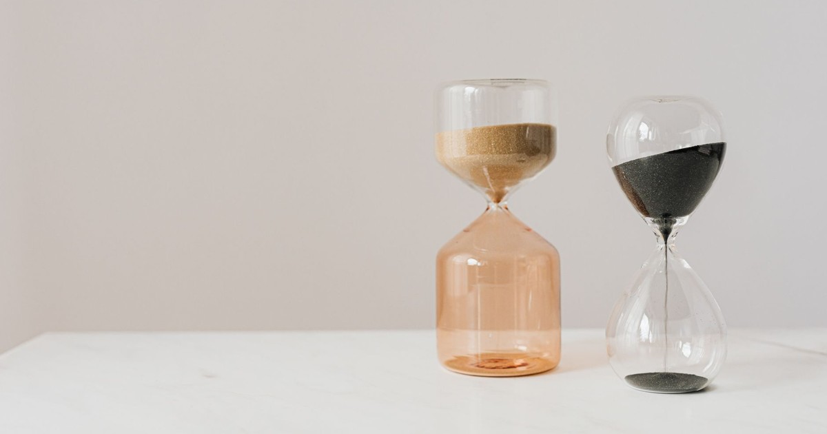 Decorative hourglasses in different shapes with pouring beige and black sand placed on white table