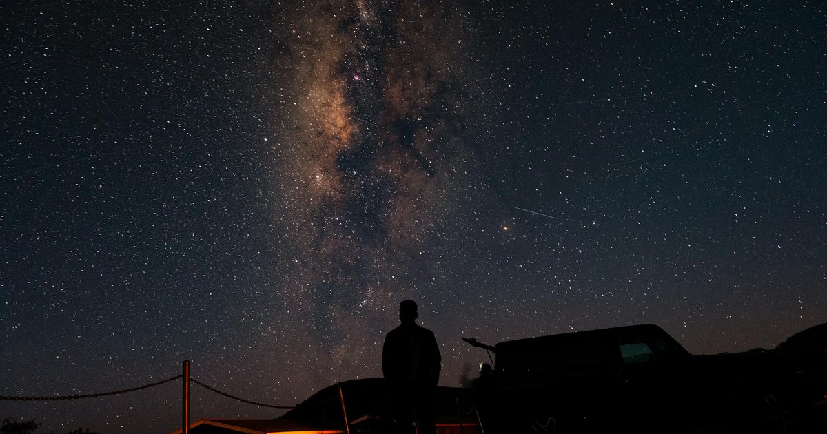 A person silhouetted against the stunning backdrop of the Milky Way and a starry night sky.