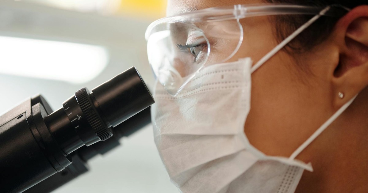 Close-up of a researcher with safety gear using a microscope in a lab.