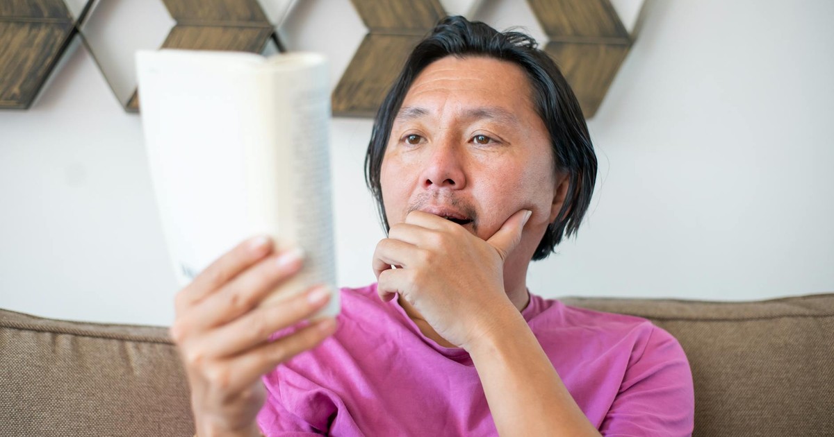 A thoughtful Asian man reading a book at home, featuring a leisure scene.