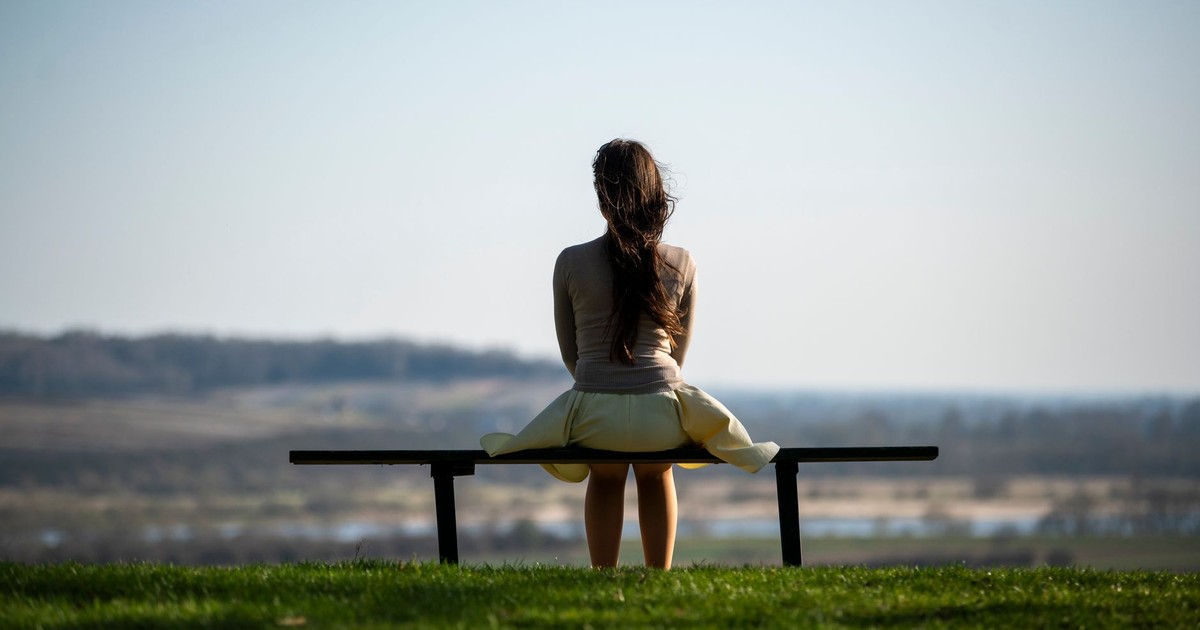 Serene image of a woman sitting on a bench overlooking a scenic field, symbolizing solitude and reflection.