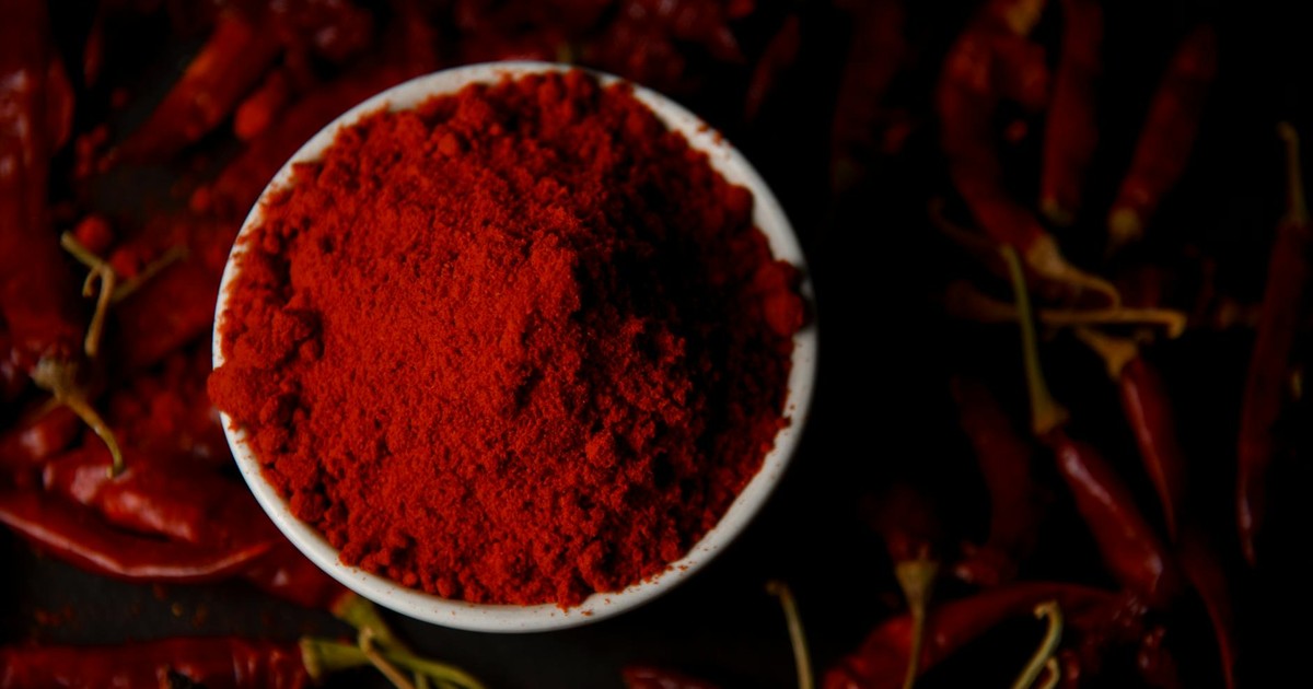 Vibrant chili powder in a bowl surrounded by dried red chilies, perfect for spice lovers.