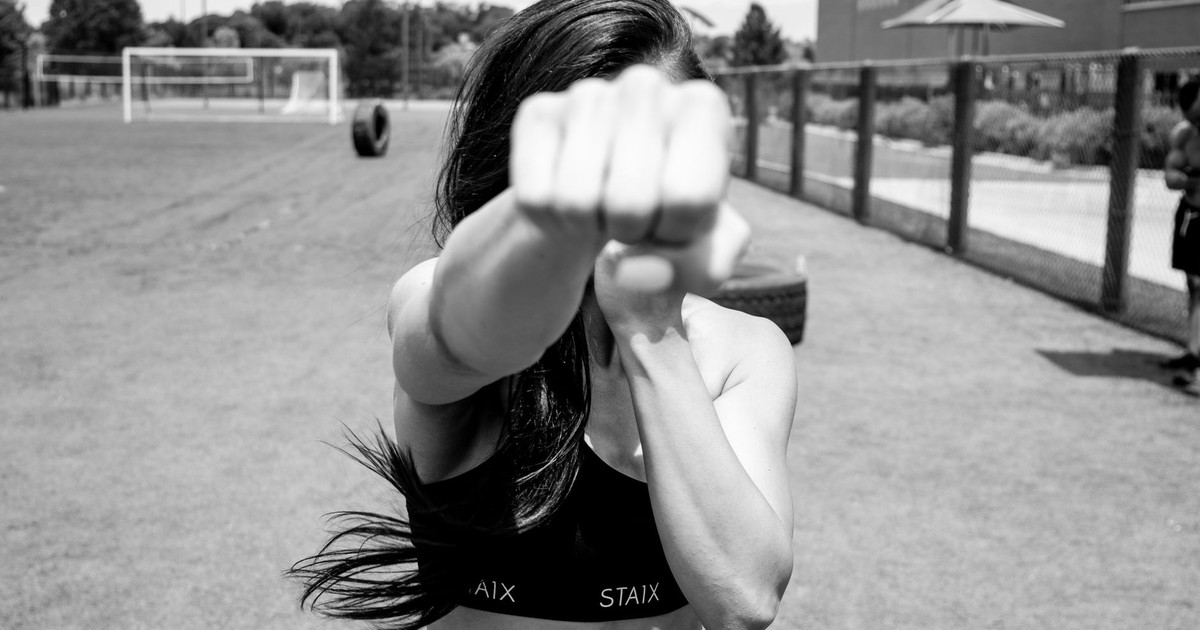 Black and white photograph of a woman punching towards the camera, showcasing strength and fitness outdoors.