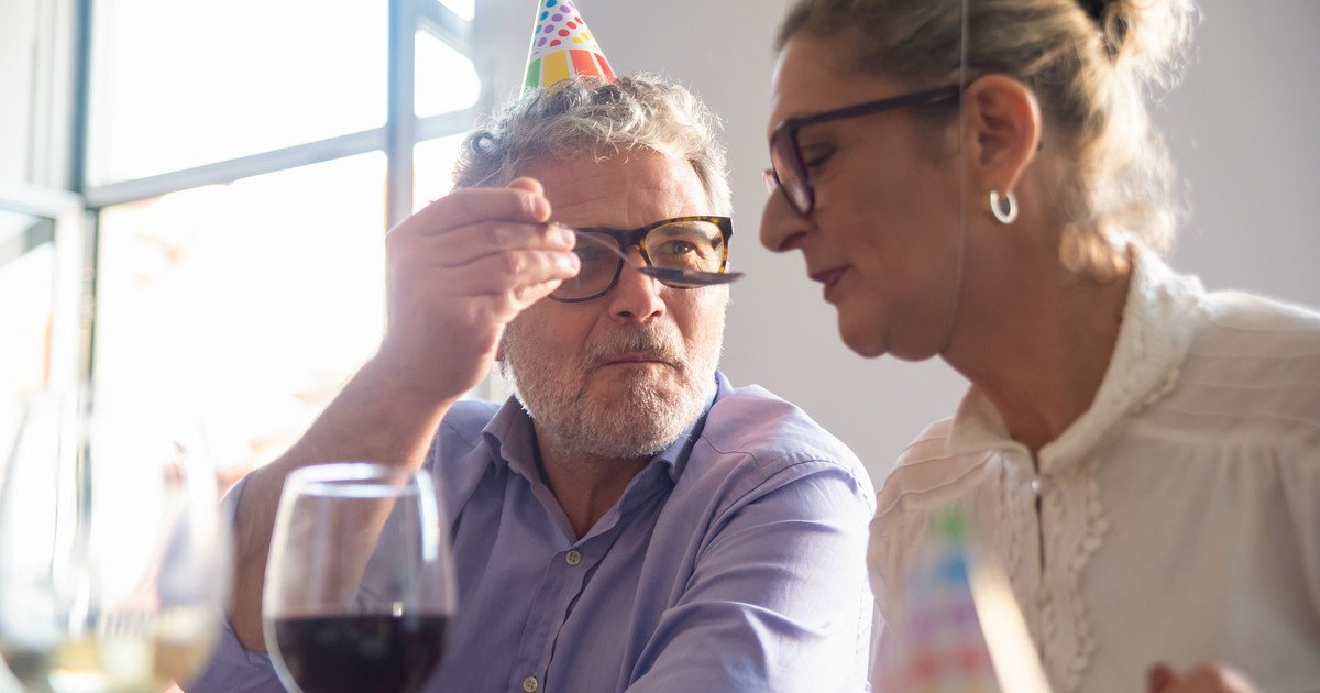 Senior couple celebrating with wine and party hats indoors, conveying joy and companionship.
