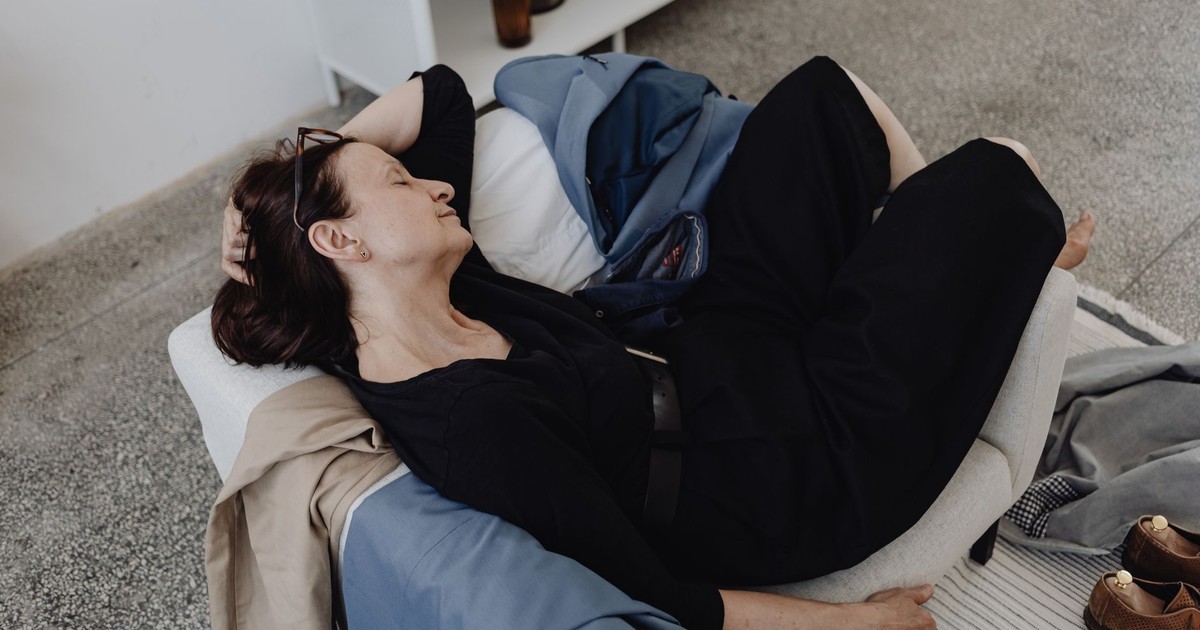 A woman rests on a sofa indoors, surrounded by casual clothing and shoes.