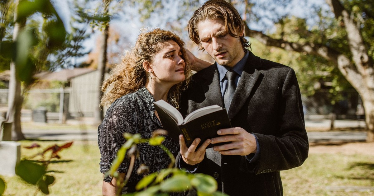 A grieving man and woman read the Bible together in a cemetery setting.