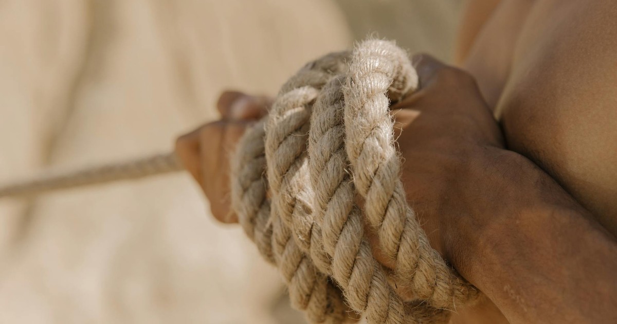 A close-up view of a person's hands tightly gripping a rope during a tug-of-war competition outdoors.