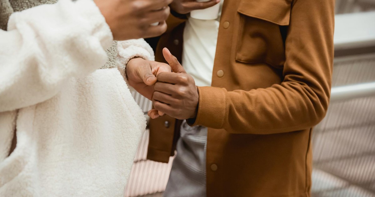 Crop faceless African American couple in trendy outfit gently touching hands while spending time together