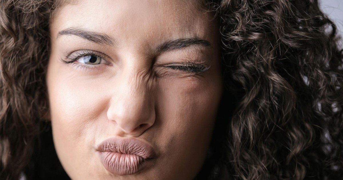 A playful close-up portrait of a woman with curly hair and a winking eye, expressing fun and mischief.