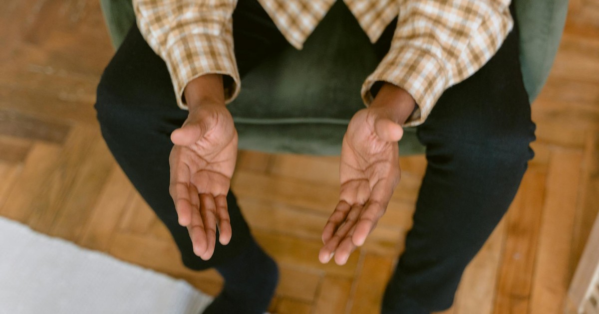 A person sitting indoors with hands open in a reflective prayer pose, inviting tranquility.