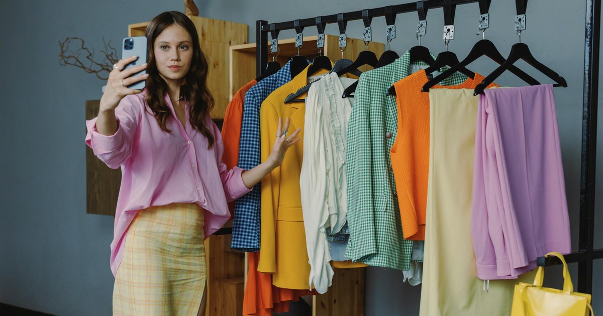 Woman in colorful outfit taking a selfie amidst vibrant clothing options in a modern boutique.