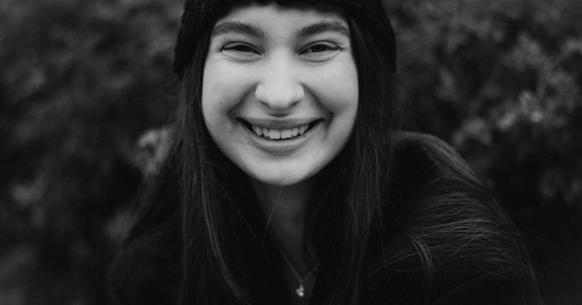 A joyful young woman smiling in a black and white outdoor portrait.