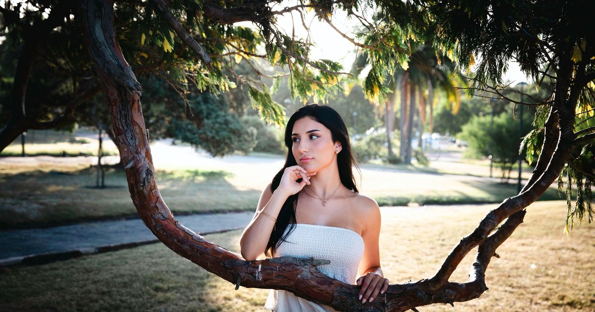 Young woman posing outdoors in sunlight framed by tree branches, capturing a serene moment.