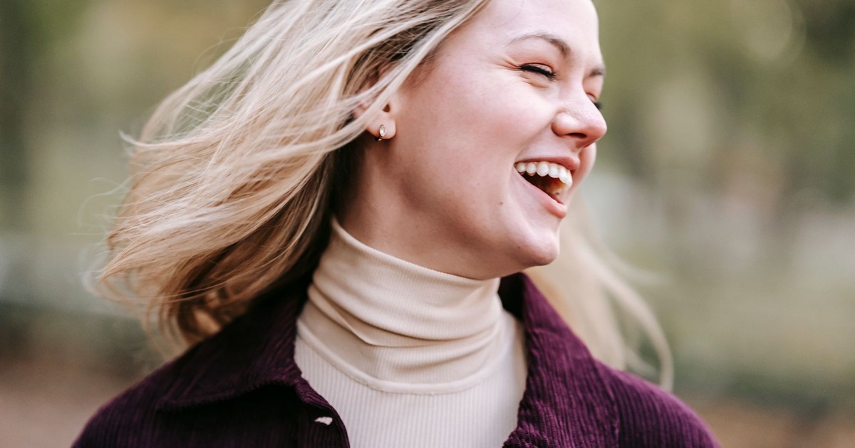 Cheerful female with flying hair and eyes closed laughing on blurred background of park