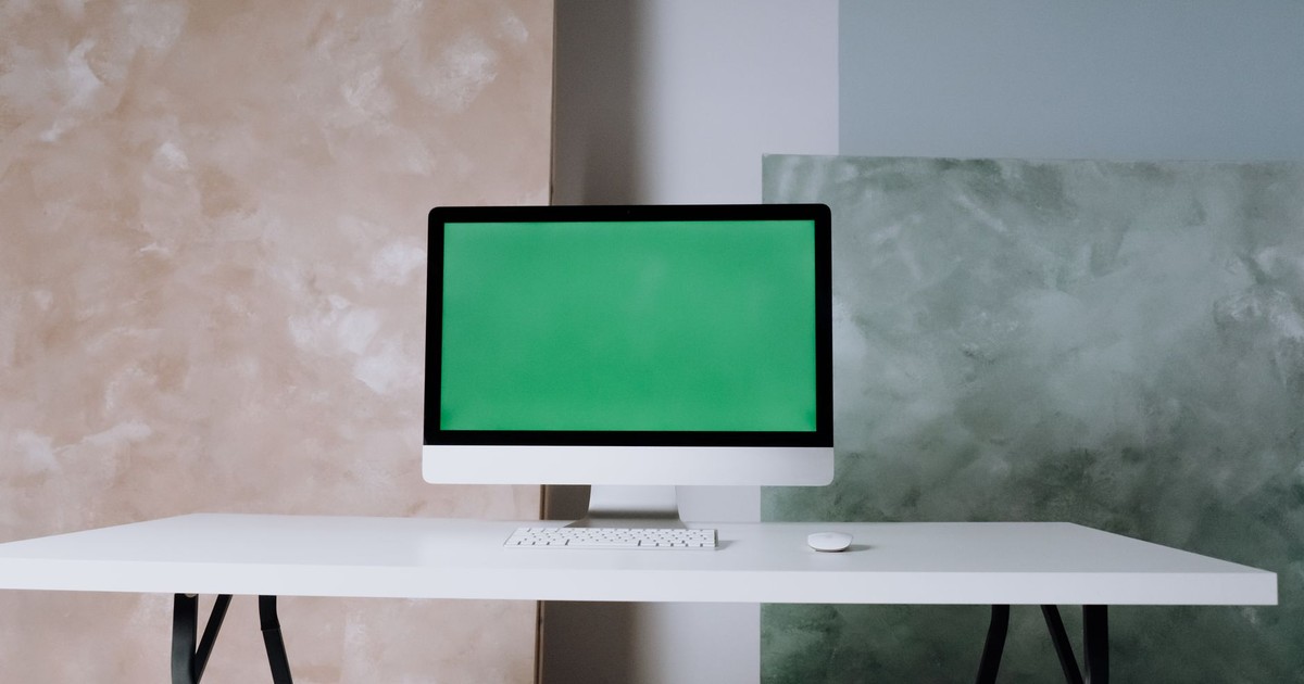 A minimalist office setup featuring an iMac with a green screen on a tidy white desk.