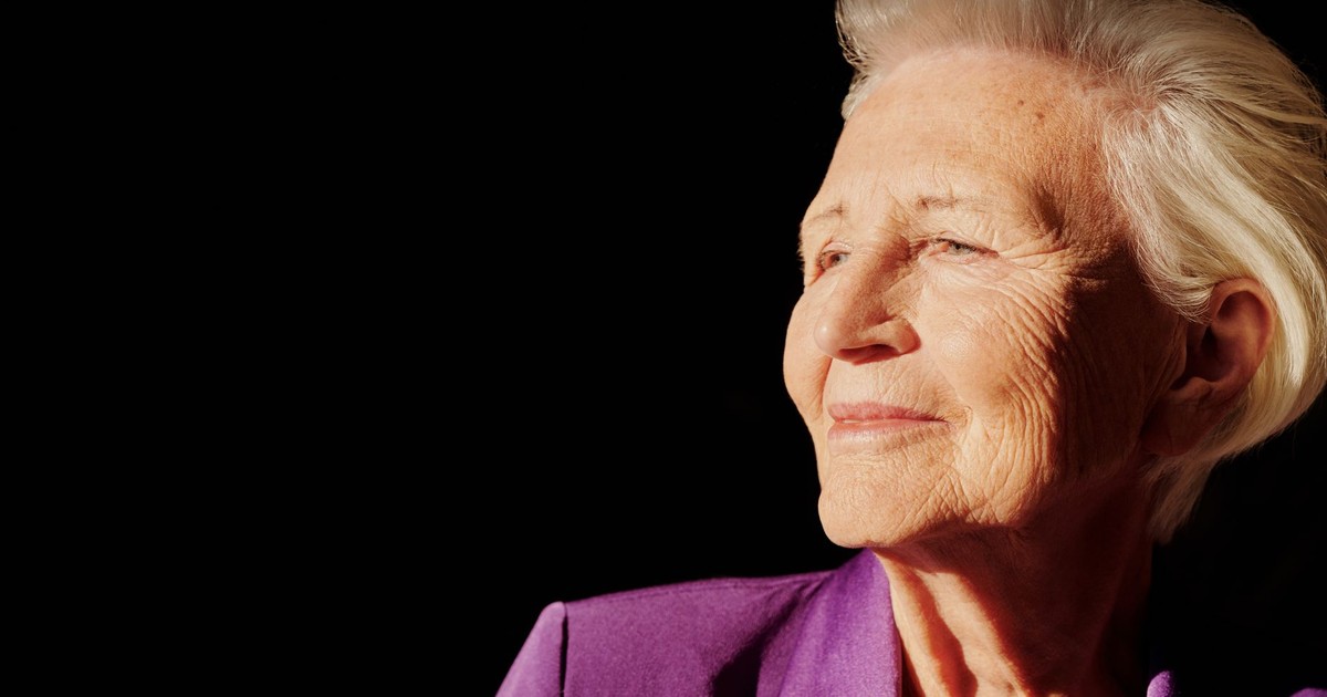 Elegant senior woman smiling with confidence in a purple jacket against black background.