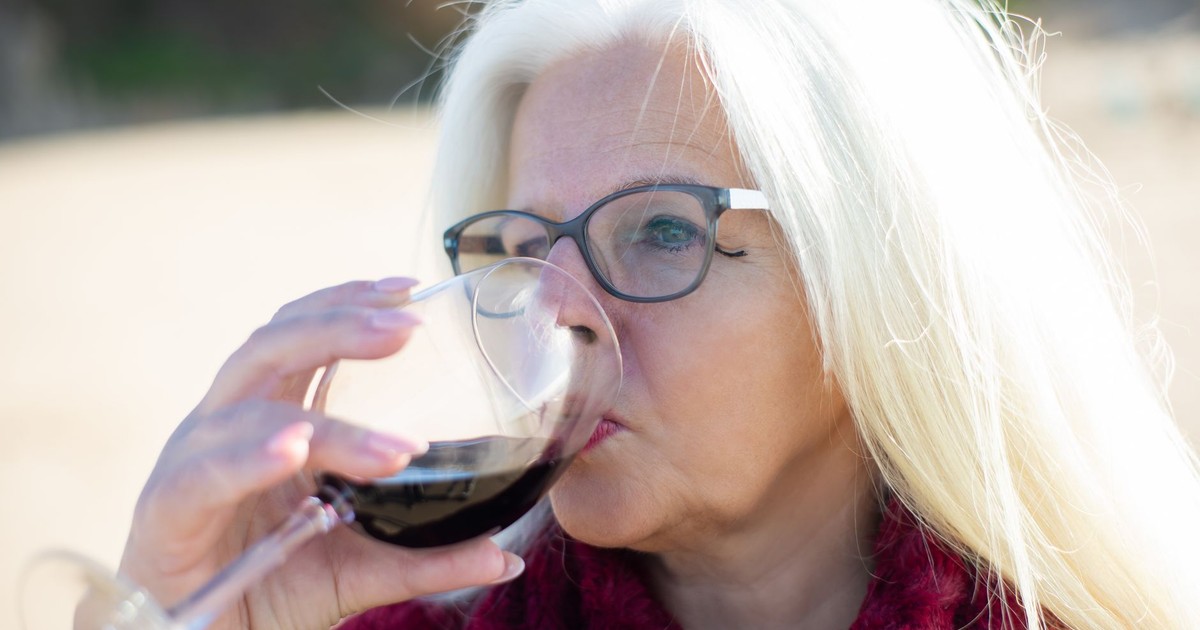 Senior woman with white hair and glasses drinking red wine on a sunny day in Portugal.