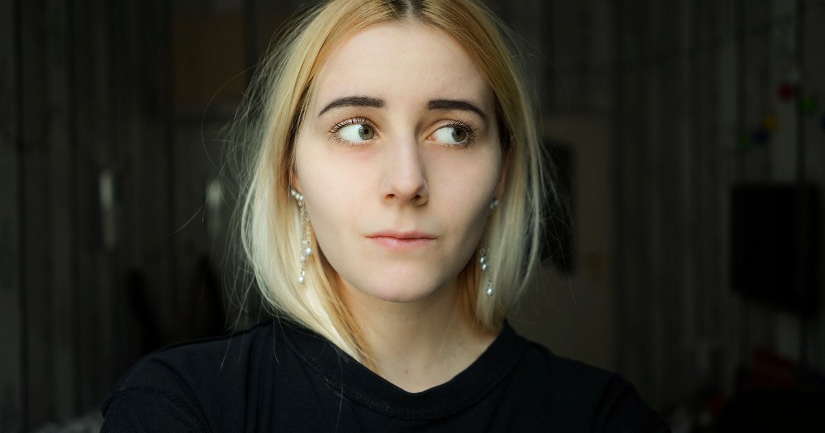 Pensive calm female in black casual outfit standing in dark room and looking away dreamily