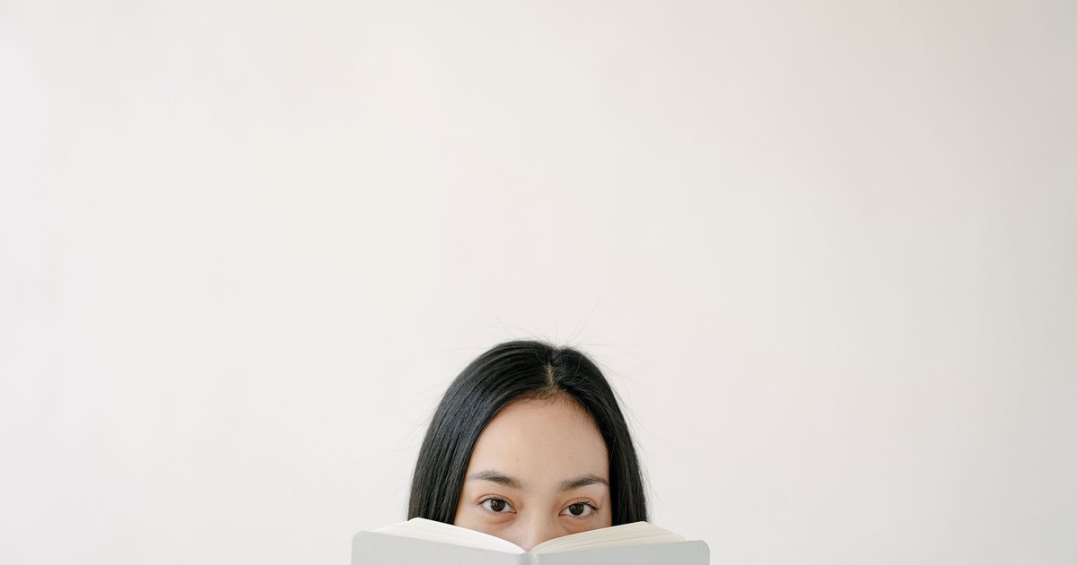 Blank wall with upper part of Asian woman face hidden behind white book