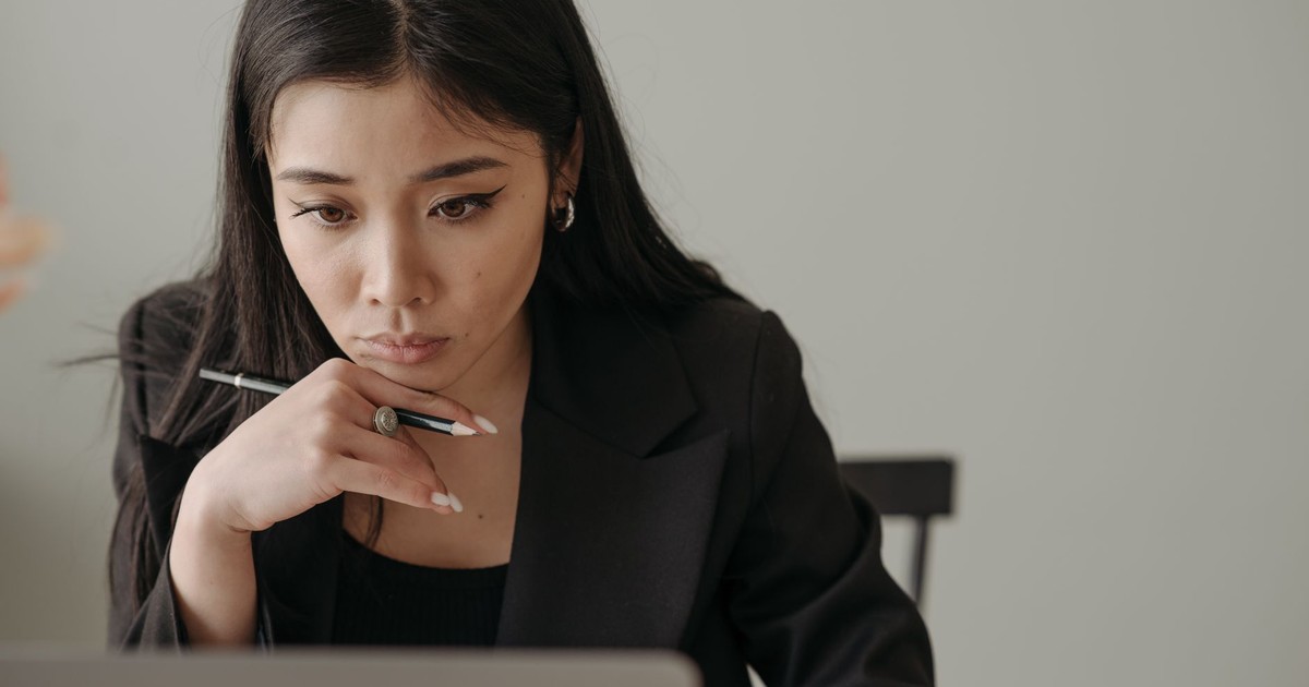 Young woman working remotely, focused on laptop in home office, holding a pencil.