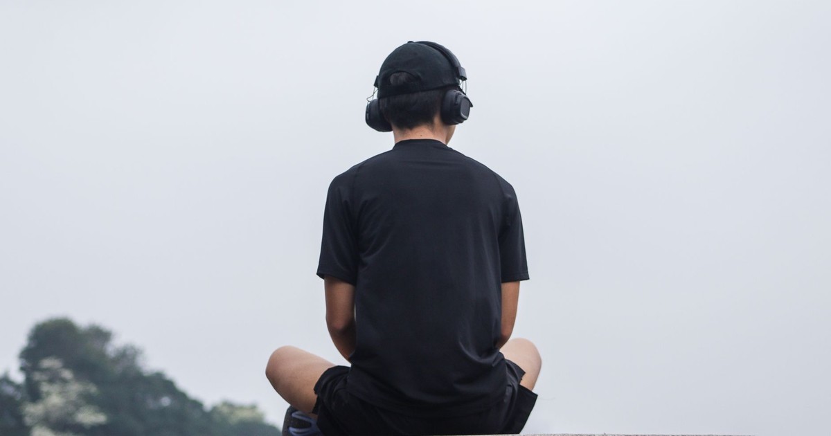 A teenager sitting cross-legged outdoors, meditating with headphones for relaxation.