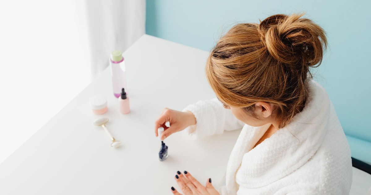 Woman in white bathrobe carefully painting her nails indoors, emphasizing self-care.